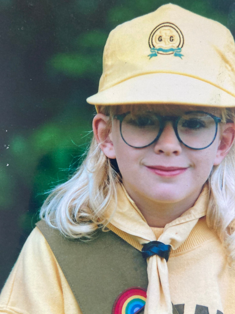 Me as a Brownie in a close-up photoshoot picture taken by my grandad. I'm wearing the 90s Jeff Banks uniform - a baseball cap, yellow sweatshirt, matching neckerchief and khaki-green sash on which you can see a little rainbow to show that I was a Rainbow.