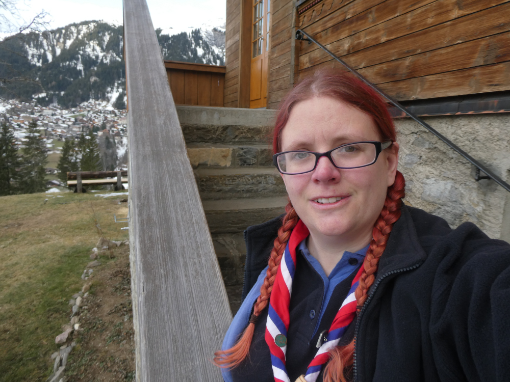 A selfie in navy leader uniform & red, white & blue international neckerchief on the back steps of Our Chalet, one of the Guide homes around the world. It's traditional to take a group picture here and we just didn't. So I did it myself as a selfie.
