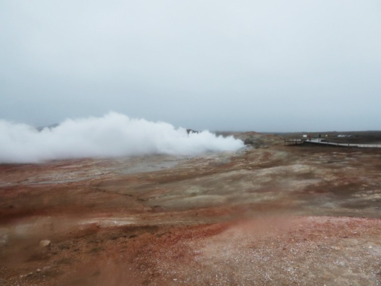 An orange and white landscape under a heavy cloudy sky - in fact, it's pouring with rain. In the middle distance is a colossal cloud of steam just billowing from a hole in the ground.