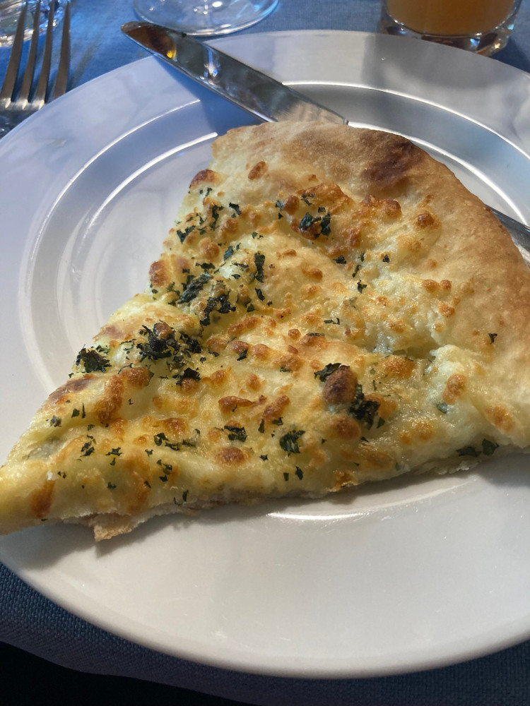 A slice of Imeretian khachapuri, a kind of Georgian cheese pizza scattered with herbs.