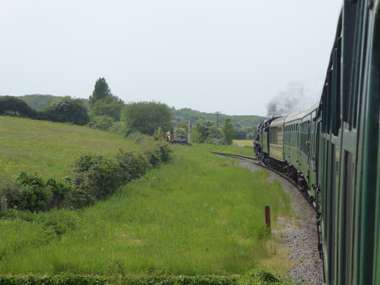 The view from a rear carriage of the Swanage Railway - a view along the train as it goes through the countryside.