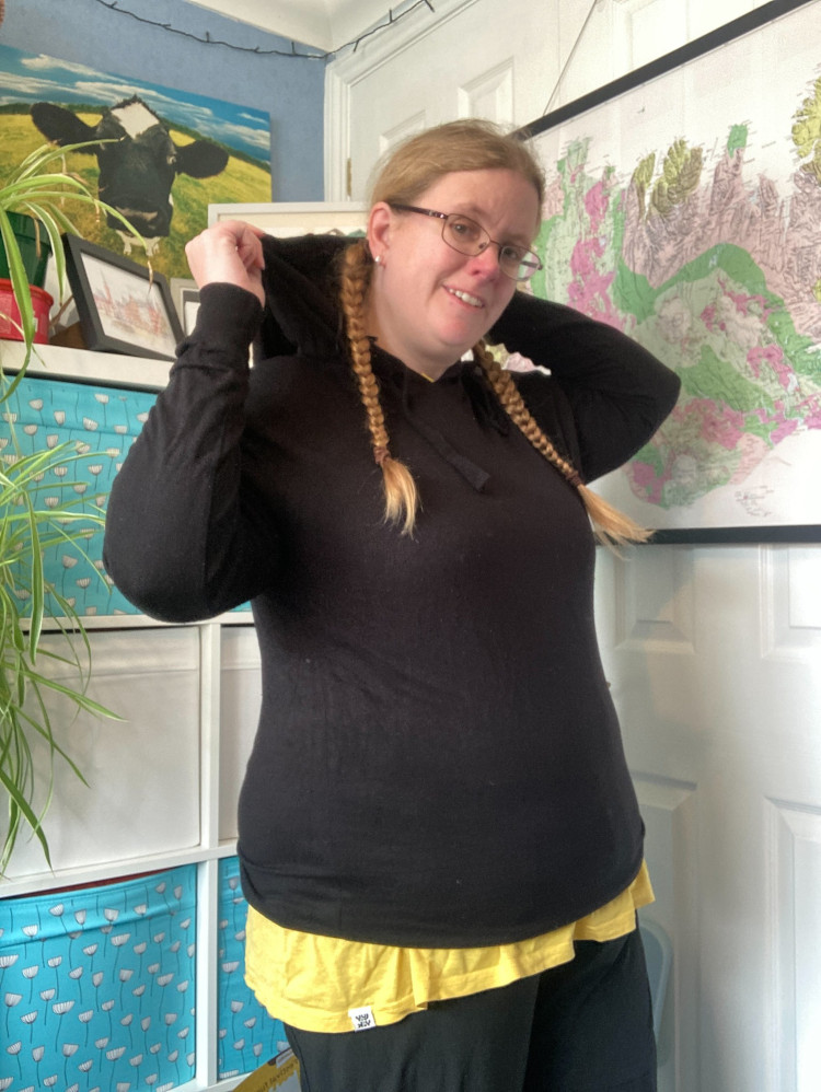 Me in my office wearing a thin lightweight black hoodie over my yellow top. I'm holding the hood up behind my head.