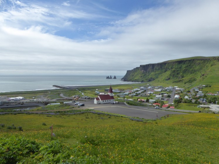 The view across Vik from above the church. The fields and cliffs are green and the sea beyond the village looks peaceful.