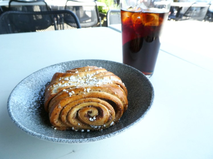 An enormous cinnamon roll and glass of Coke on a table outside Helsinki's big tourist sauna.