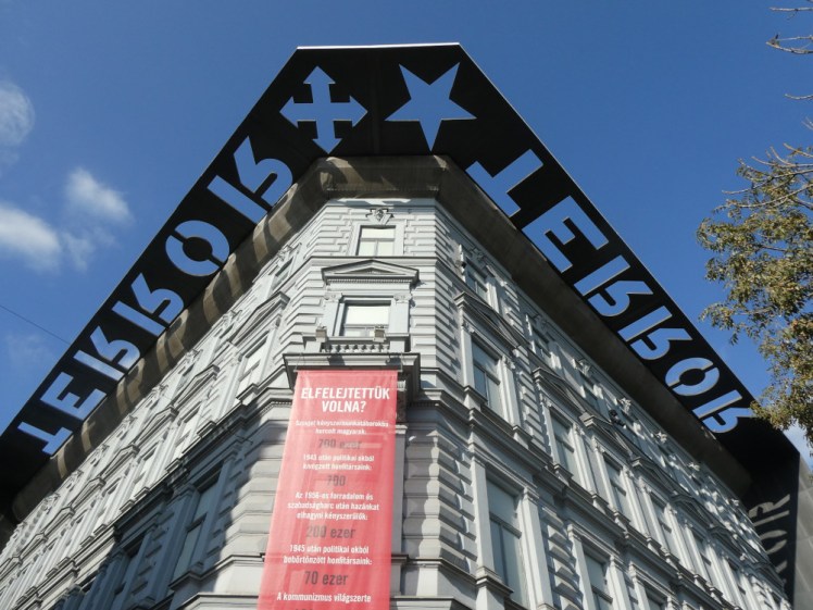 The House of Terror, a neo-Renaissance building with a black shade along the top, the word TERROR cut out so it it forms shadows on the top of the building during the afternoon.