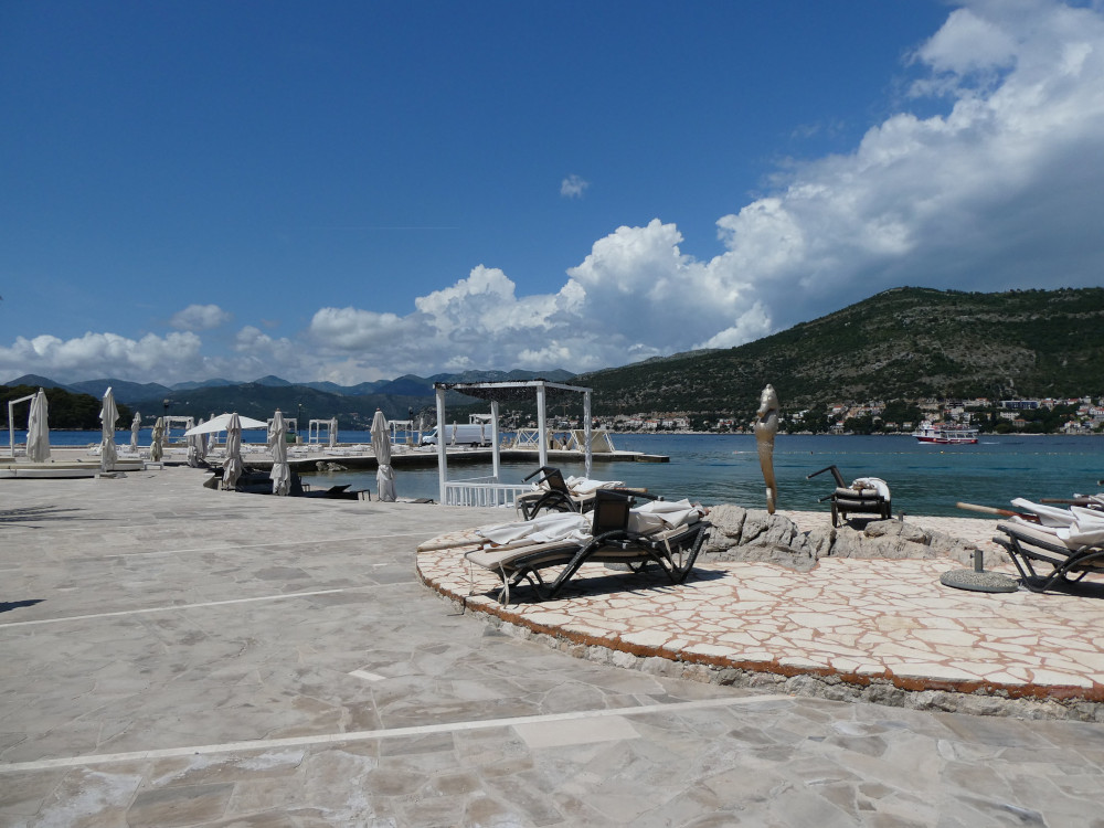 The beach club side of the beach, with umbrellas and sun loungers on a stone seafront overlooking the bay.