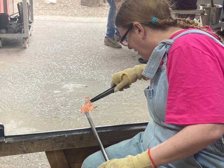 Me, in denim dungarees and a bright pink t-shirt, pulling at a glob of glass with a pair of overgrown tweezers, shaping it into a kind of explosion.