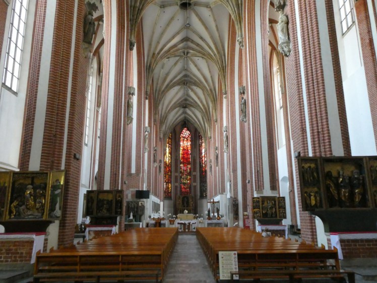Inside the Catholic Church as seen from the door - the place is all white with pinkish brick pillars up to a plain vaulted ceiling. In the distance is an amazing red stained glass window.