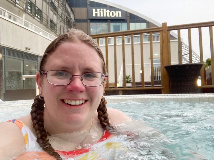 A selfie in the hot tub out on the deck. You can see the curve of the torus-shaped hotel behind me and a huge Hilton logo on the side of it.