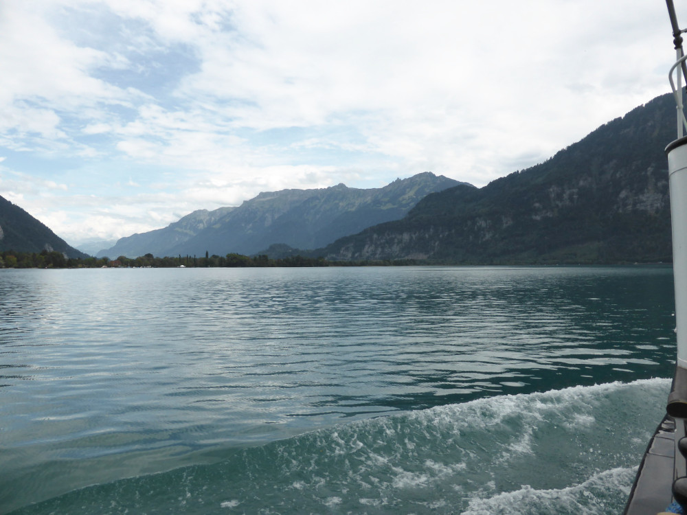 A view across the lake from the boat. You can see the boat's wave sweeping down the side. The sky is pretty blue behind some clouds but it's quite dark on the water.
