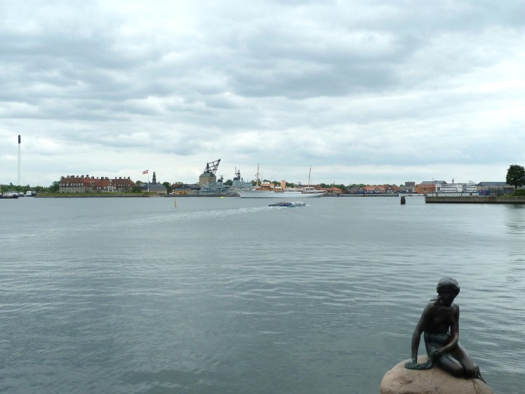The Little Mermaid statue sits on her rock in the corner of the photo, Copenhagen's rather industrial harbour behind her.