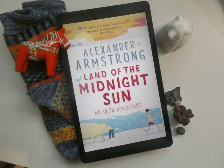 Alexander Armstrong, Land of the Midnight Sun. Book cover on my tablet. The cover is mostly white, with a yellow sunset across the top and a picture of a man in tiny red shorts running away from a polar bear holding his trousers in front of the sea at the bottom. The author's name is in blue capitals and the book title is in red, all with really annoying shadows underneath that make it look faintly blurry even though it's not.