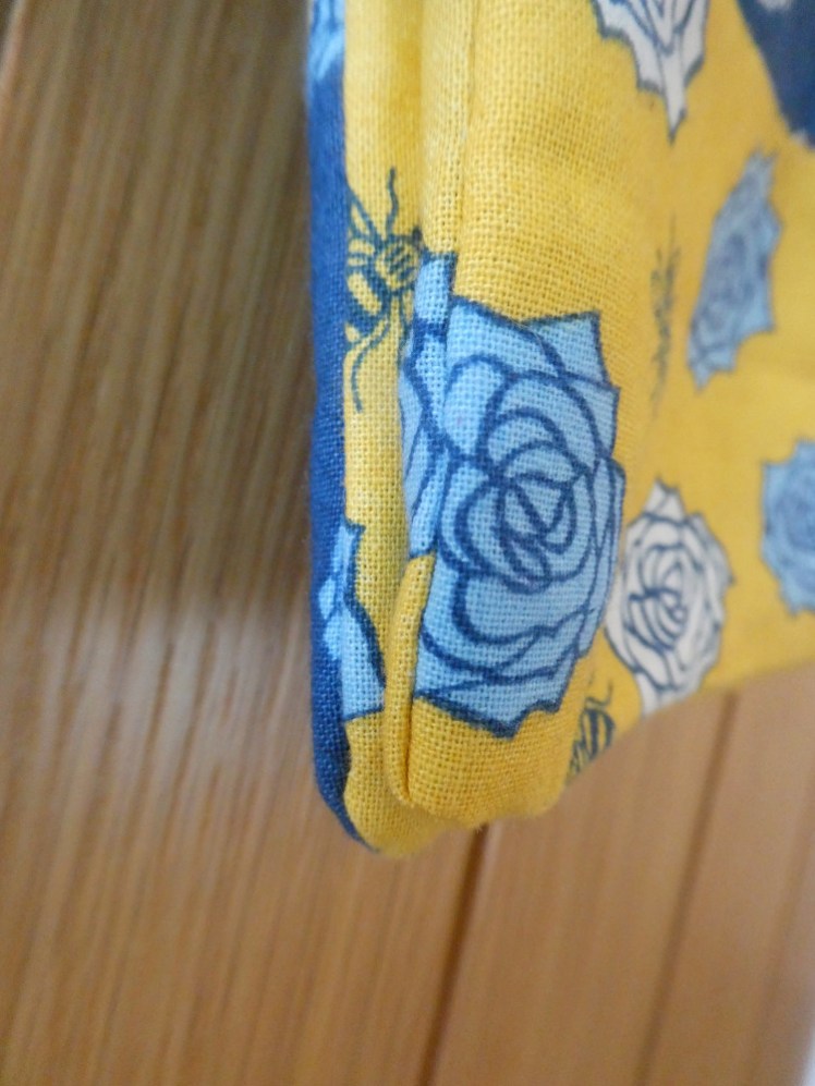 The bottom corner of the bag, showing two pouches, both in yellow with blue flowers and bees and the back in a dark blue fabric.