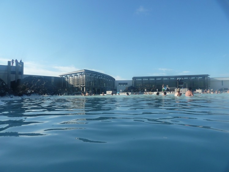 In the Blue Lagoon, low in the water, looking towards the facility's own glass buildings, housing the changing rooms, restaurant, cafe and so on.