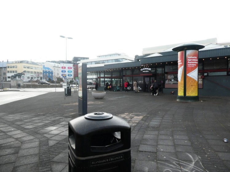 Hlemmur bus hub, a series of bus stops marked by a board of bus number boards, arranged around a single-storey building that's now a food hall.