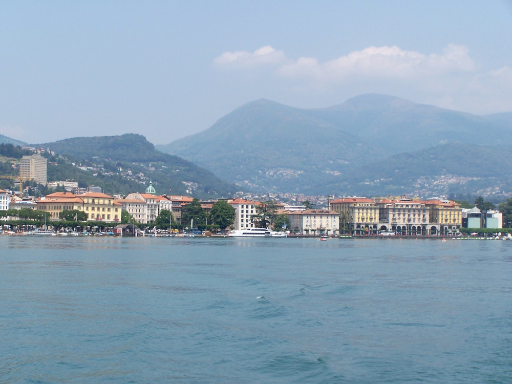 Lugano from the water: lots of large square buildings with red roofs and pastel walls.