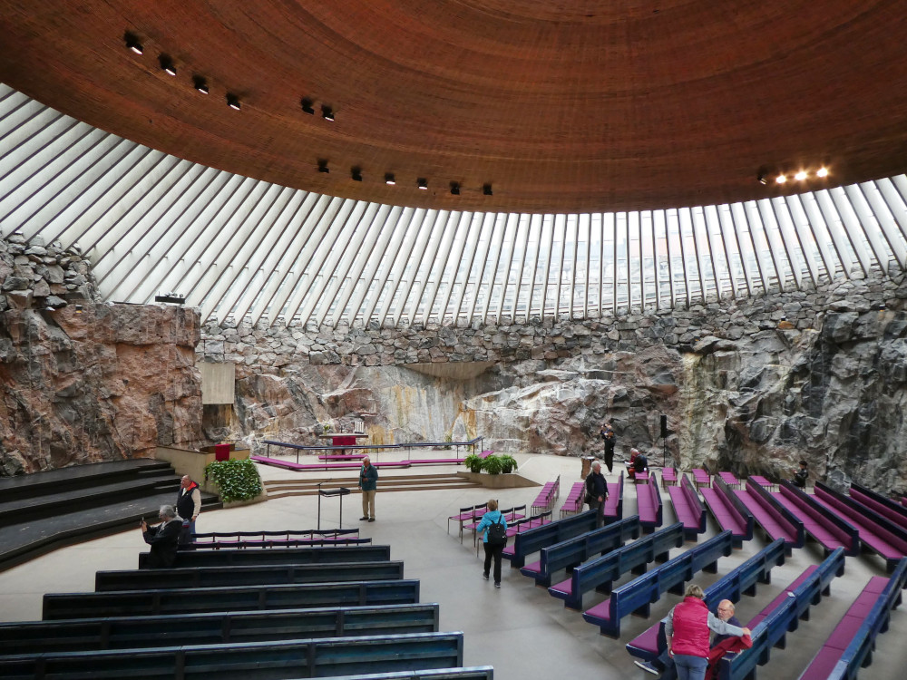 Inside the Church in the Rock, a circular space with rough raw rock walls reaching about one storey high. Above them is a flat copper dome supported by concrete pillars which let in outside light.
