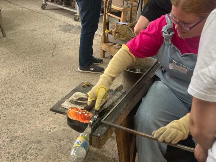 Shaping the paperweight with a wooden block, rolling a lump of molten orange glass in a kind of wooden cup on a stick.