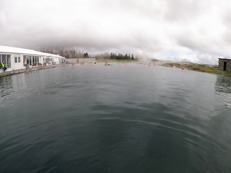 The Secret Lagoon. Around the edges are the service building on one side and a brick outhouse on the other. At the back is a fenced off area that's steaming enthusiastically - it's one of the hot springs that provides the hot water.