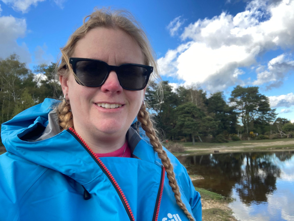 Selfie standing by a pond that doesn't have a single ripple marring its perfect reflection of the sky above. I'm wearing a bright blue waterproof jacket with a protective flap underneath the half-zip, which I've left undone.