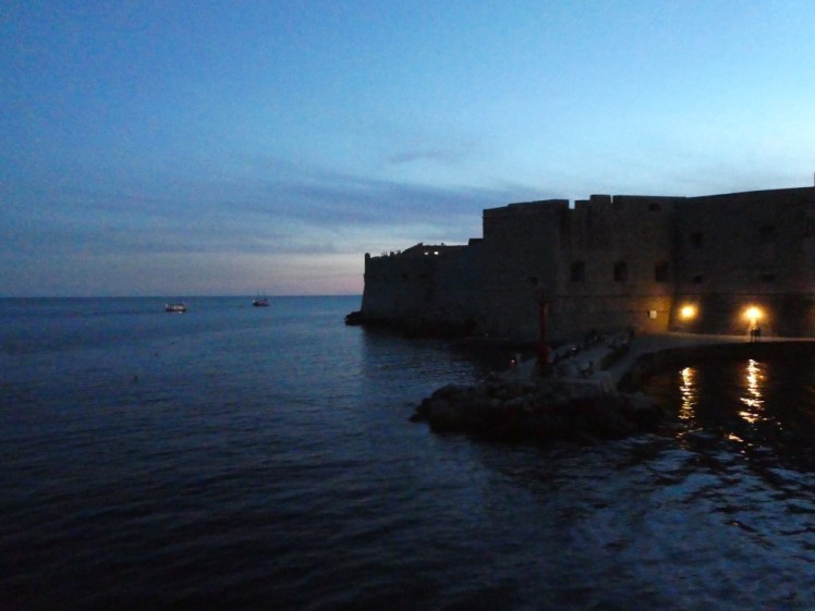 The imposing stone walls of Dubrovnik's Old Town, seen from a little way offshore at about the height of the walls. It's a bit dark so the walls are fairly well shadowed but you can make out details of bricks and windows.