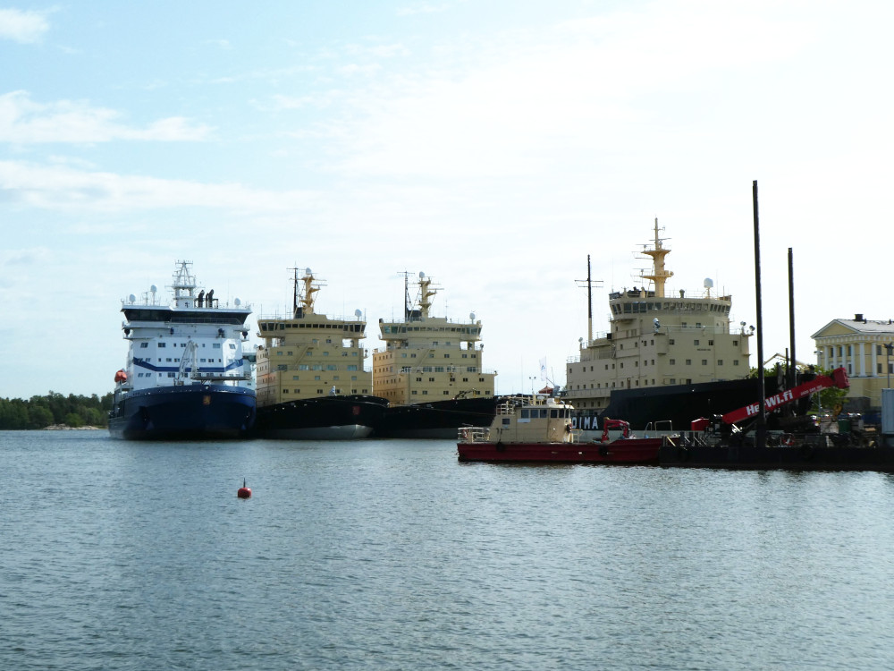 Finland's icebreaker fleet. Five or six large boats with huge chunky block-like towers set on very sturdy hells. Most of them are yellowish with black bottoms. One visible and one hiding have dark blue bottoms and white towers with swoops of Finnish blue.