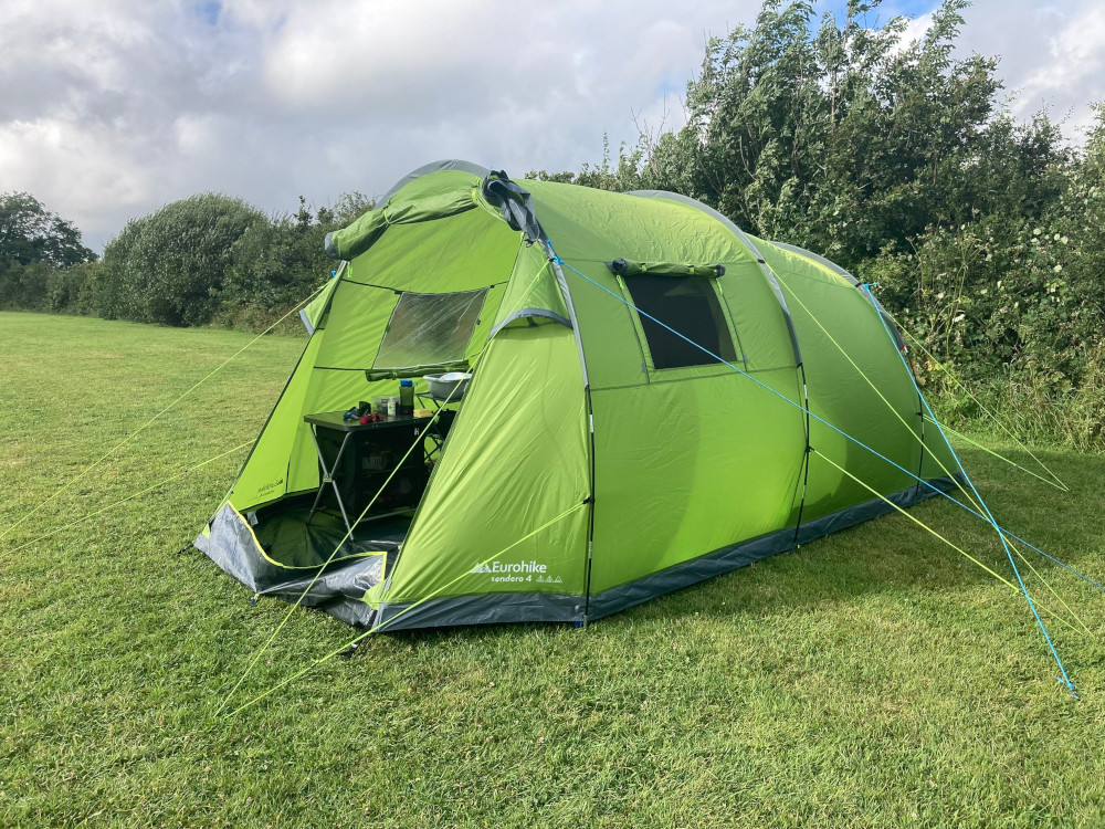 My big green 4-man tent standing alone in a grassy field with a hedge running along the back.