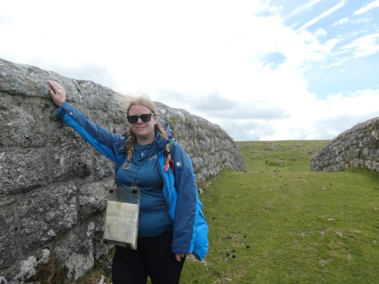 Me, on a grass-covered bridge on Dartmoor, wearing a blue waterproof jacket, a blue base layer, hiking trousers and a map in a plastic case around my neck.