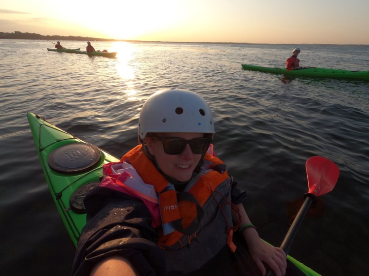 A selfie in the kayak, all dressed up in my waterproof kit, with the low sun behind me and my fellow paddlers silhouetted.