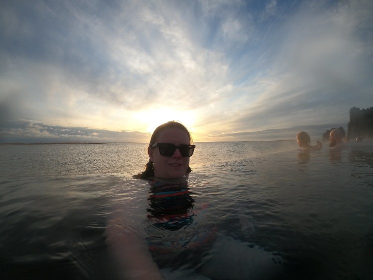 Me in Iceland's Sky Lagoon by the infinity edge with a pale yellow and blue sunset behind me