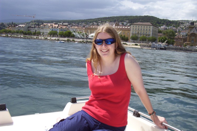 Me, aged twenty, on the back of a boat on Lake Neuchatel. My hair is down for once and slightly more golden-blonde than it is these days. I'm wearing a red vest and big blue shiny sunglasses. Behind me is a city made of yellow sandstone clustered at the foot of a mountain and behind that is a huge black sky that we on the boat clearly haven't noticed yet.