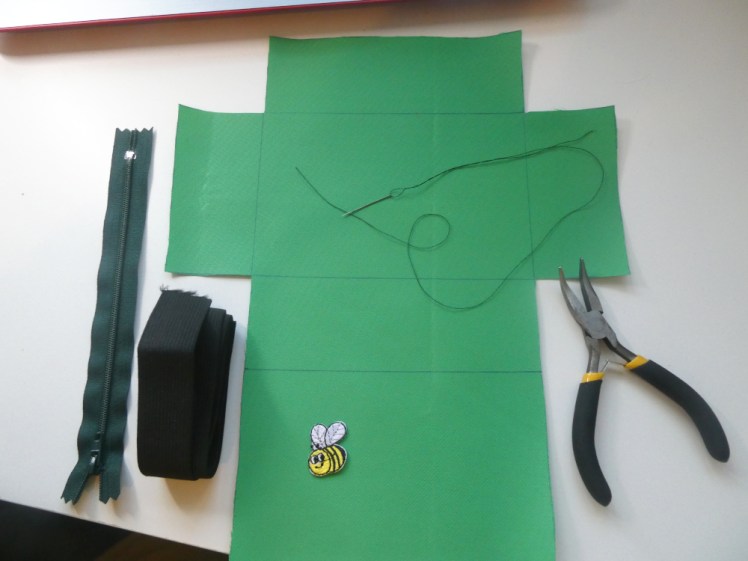 My materials laid out: a dark green zip, a roll of black 20mm elastic, my cordura, a needle and thread, a pair of pliers and a little iron-on bee motif for a finishing touch.