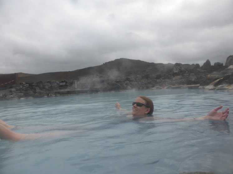 Me floating in the Nature Baths with my arms out. Behind me, a reddish mountain rises up out of the boulders that edge the lagoon.