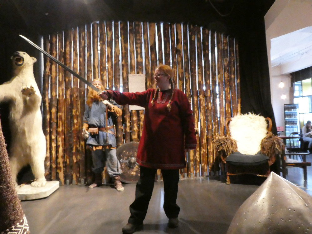 Me in a red Viking tunic with gold trimming, holding a longsword out to my right. The photo isn't really in focus because I used the timer selfie mode in a dimly lit room.