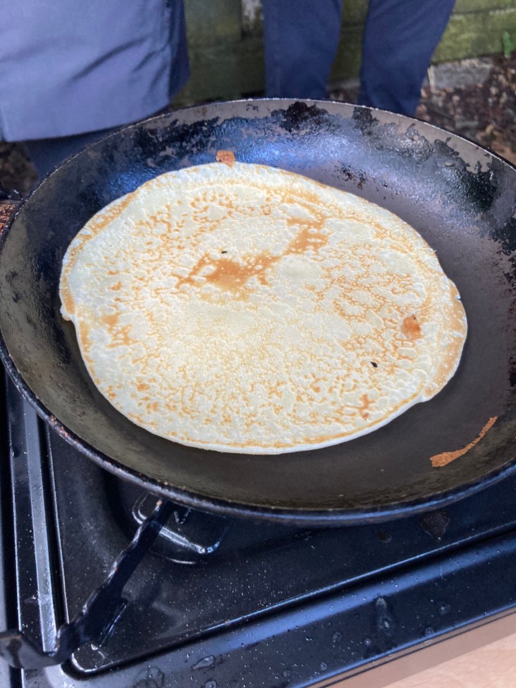 A beautiful pancake in a pan over a gas stove outside.