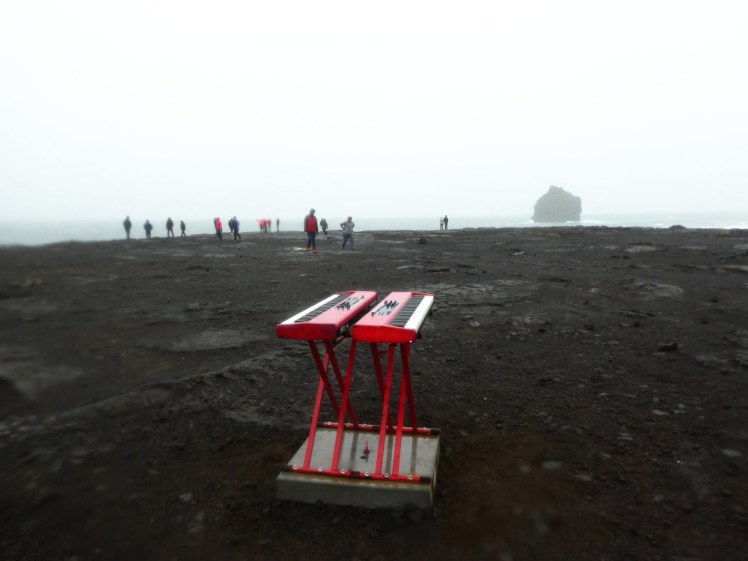 A patch of desolate grey rock gives way to a grey sea, all overhung by heavy mist. The scene is wet and miserable. In the middle is the double red keyboard thing from the Eurovision Iceland movie that I haven't seen.
