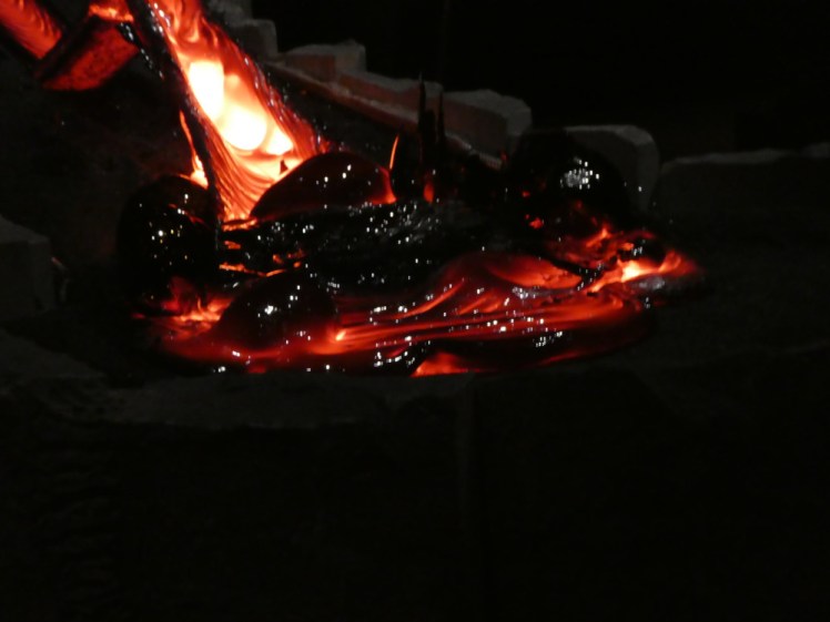 Cooled black lava bubbles with the yellow-hot slide in the background.