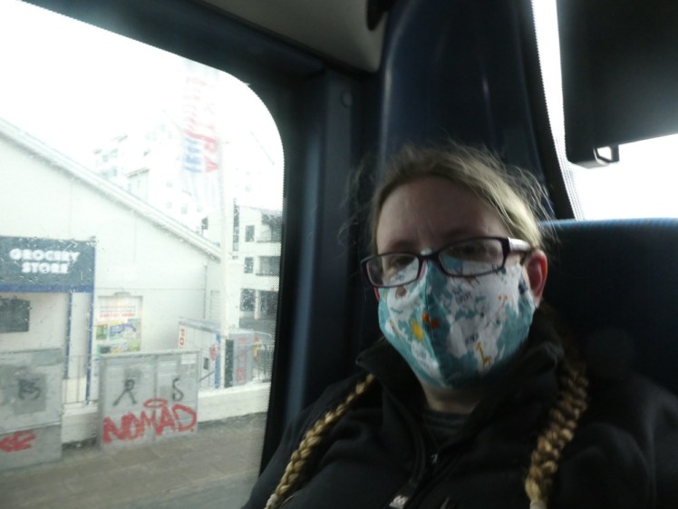 Selfie on the bus - me sitting in the back seat wearing a mask with a cartooon-style map of the world on it.