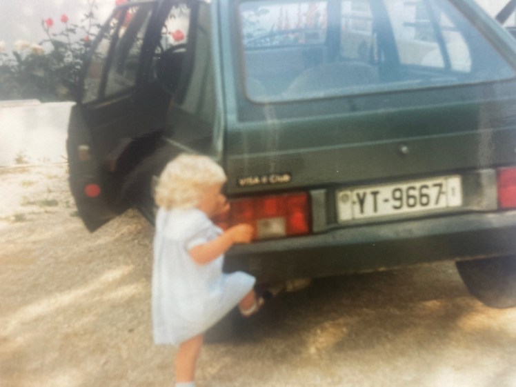 Tiny me, in a little blue dress, kicking the bumper of the hire car, which is about waist-height on me.