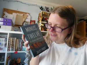 Me holding up my book and looking utterly in love. It's a small paperback with a blue sky and a sunset-lit mountain range.