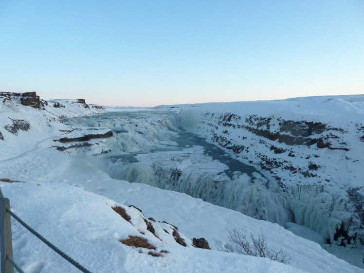 Gullfoss, a large two-step waterfalls, almost completely frozen over. Its steep banks are all snow and its roaring falls are all fluffy ice.