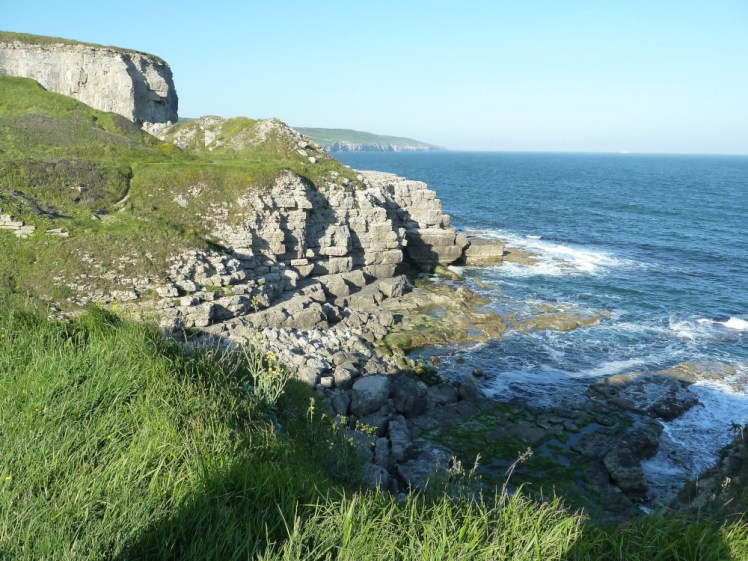The sea in a rock-strewn bay surrounded by craggy cliffs. The sea is very blue but it's still far too scary to swim.