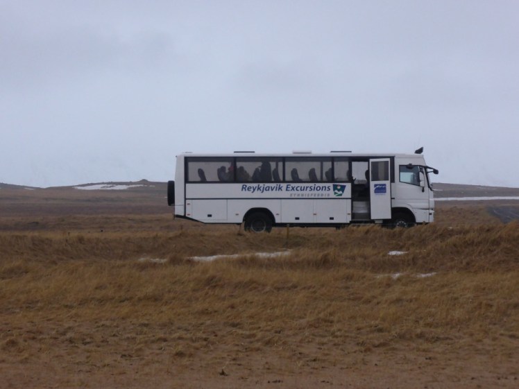 A Reykjavik Excursions bus parked on Snæfellsnes, with a grey winter sky above and an orange-brown field of what's probably just long grass in summer.