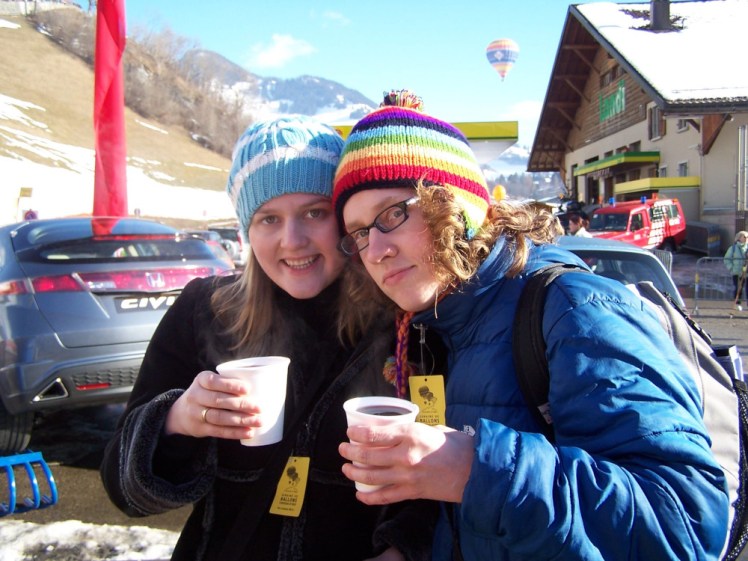 My "triplets" - Jemma is wearing a blue and white striped hat and black coat, Angela is wearing the rainbow hat and a blue puffa jacket. Both are wearing the yellow labels/tickets and holding plastic cups of hot wine.