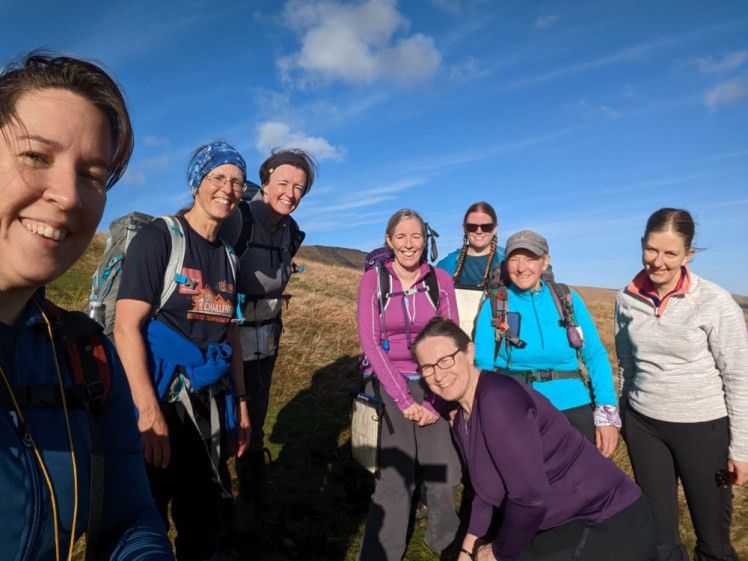 Group photo before we split up: eight women with backpacks and fleeces on a hillside. Behind us, you can see the ridge of the mountain we're going to climb.