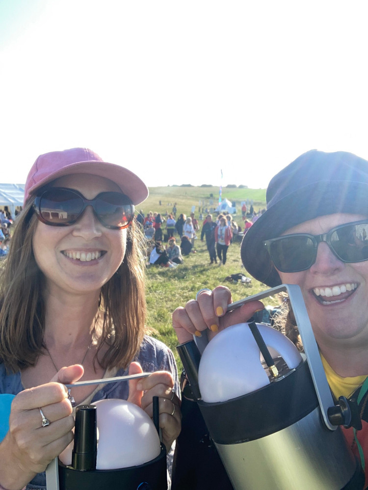 A selfie with me and Catherine. We're both wearing sunglasses and the sun is directly behind me. Catherine is wearing a pink cap, a blue t-shirt and you can just make out her Team Light Blue sticker. We're both holding up our Geolights, which are aluminium canisters with metal handles and a white plastic dome on top.