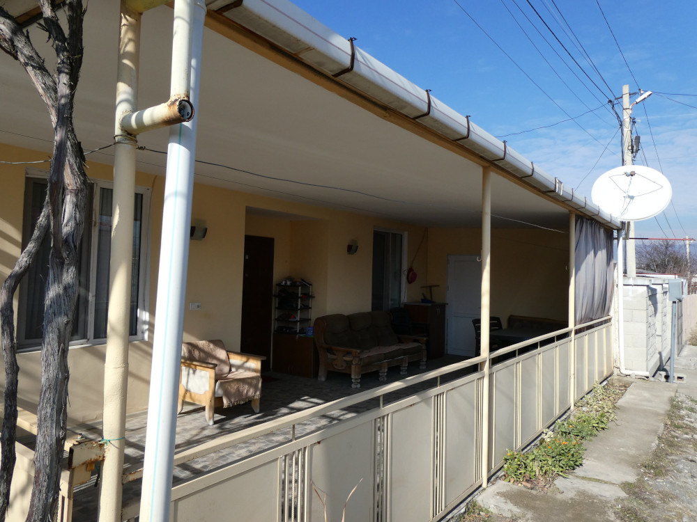 A house with a porch, a chicken coop and a satellite dish. This house is painted an apricot shade of yellow instead of the battered pink and white of many of the others and has a fence along the front.