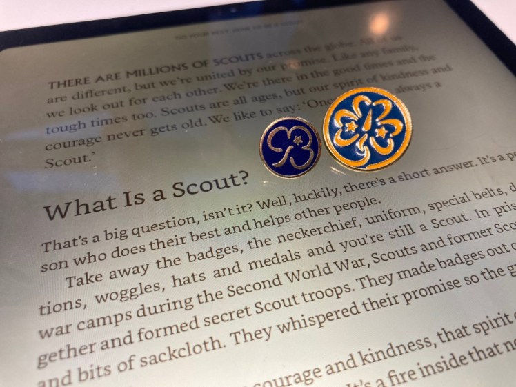 A close-up of a sub-chapter titled What Is A Scout? My miniature adult Promise badge and a WAGGGS member badge are lying on the tablet next to the title.