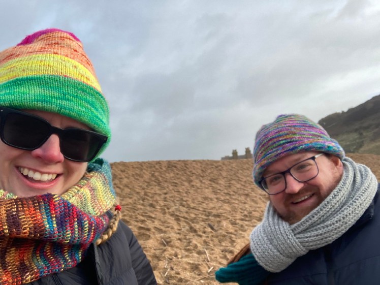 Selfie with me and Tom in it, both of us wearing our colourful hats and scarves on top of the shingle bank at West Bay.
