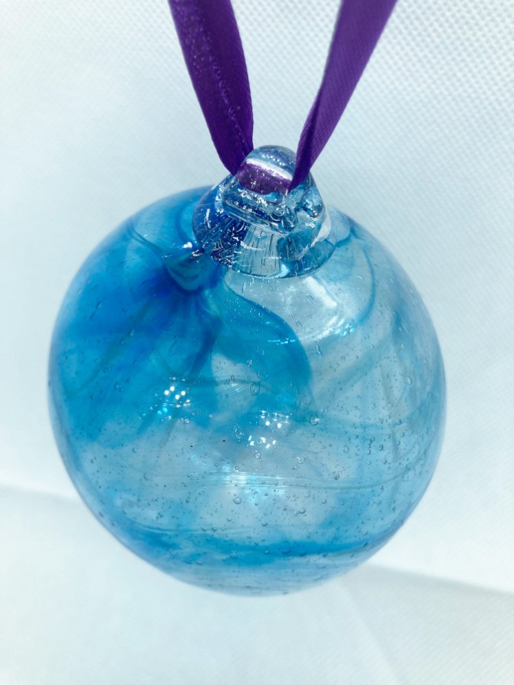The finished bauble. An inflated bauble nearly four inches in diameter with translucent blue swirls in it. It's hanging from a loop of deep purple ribbon.